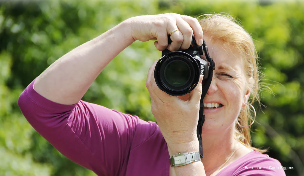 Vrouw met de camera voor het oog tijdens de basiscursus Fotografie.